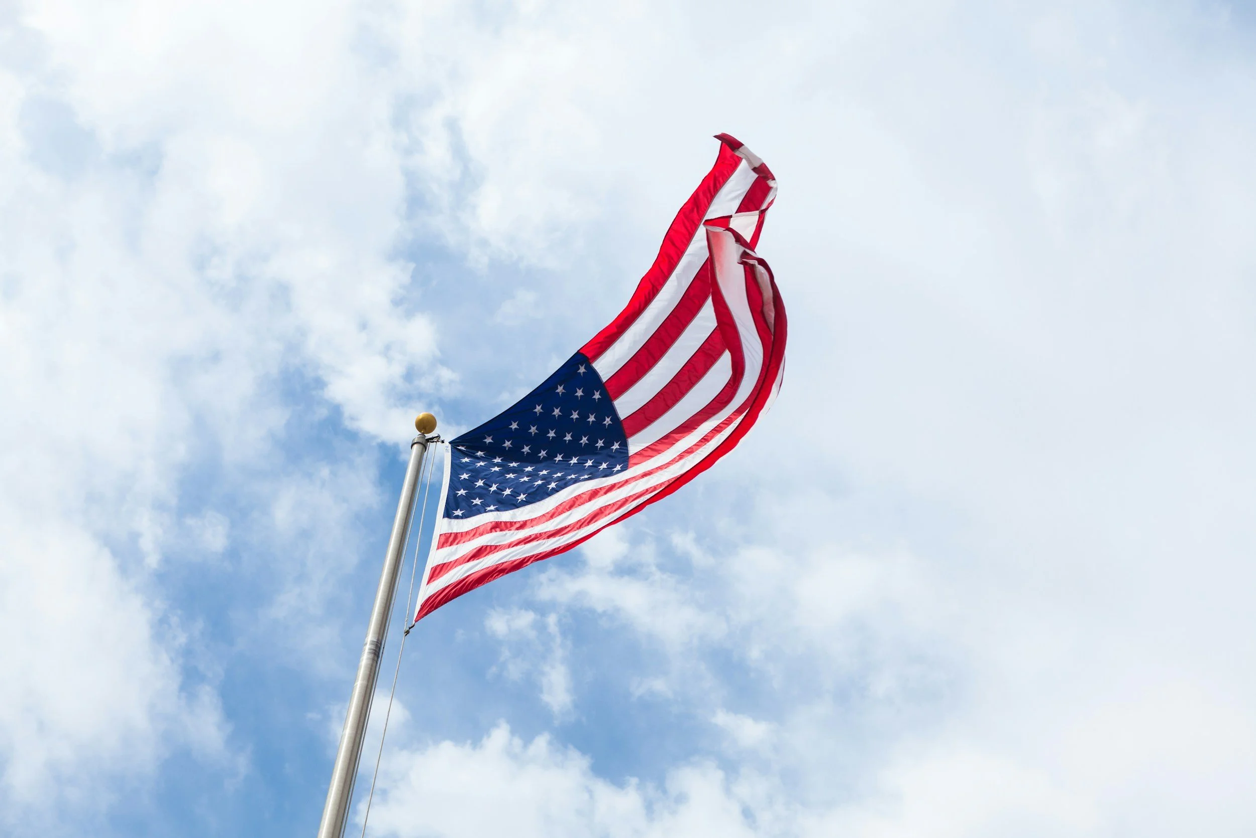 American flag flying against a partly cloudy sky.