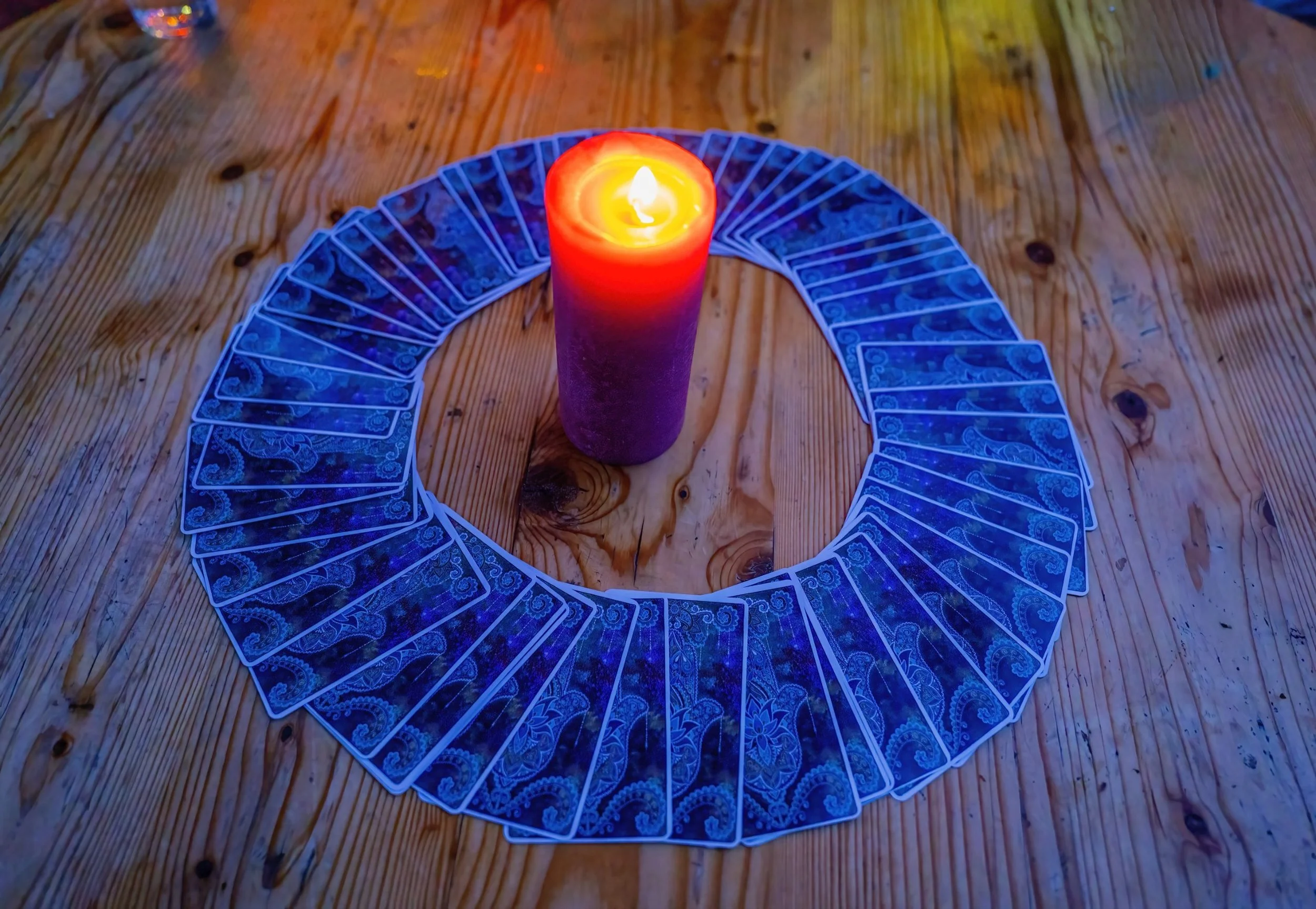Ein Deck aus Spielkarten ist kreisförmig um eine brennende Kerze auf einem Holztisch angeordnet.