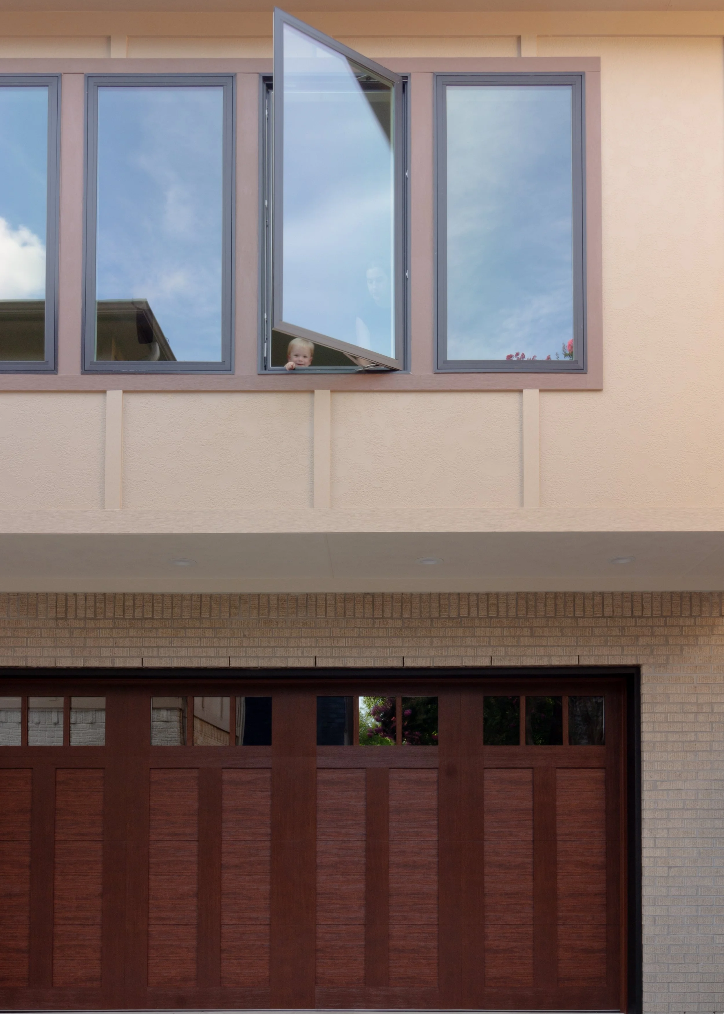 A back house with large windows and a closed wooden garage door. One of the upper windows is open with a child peeking out.