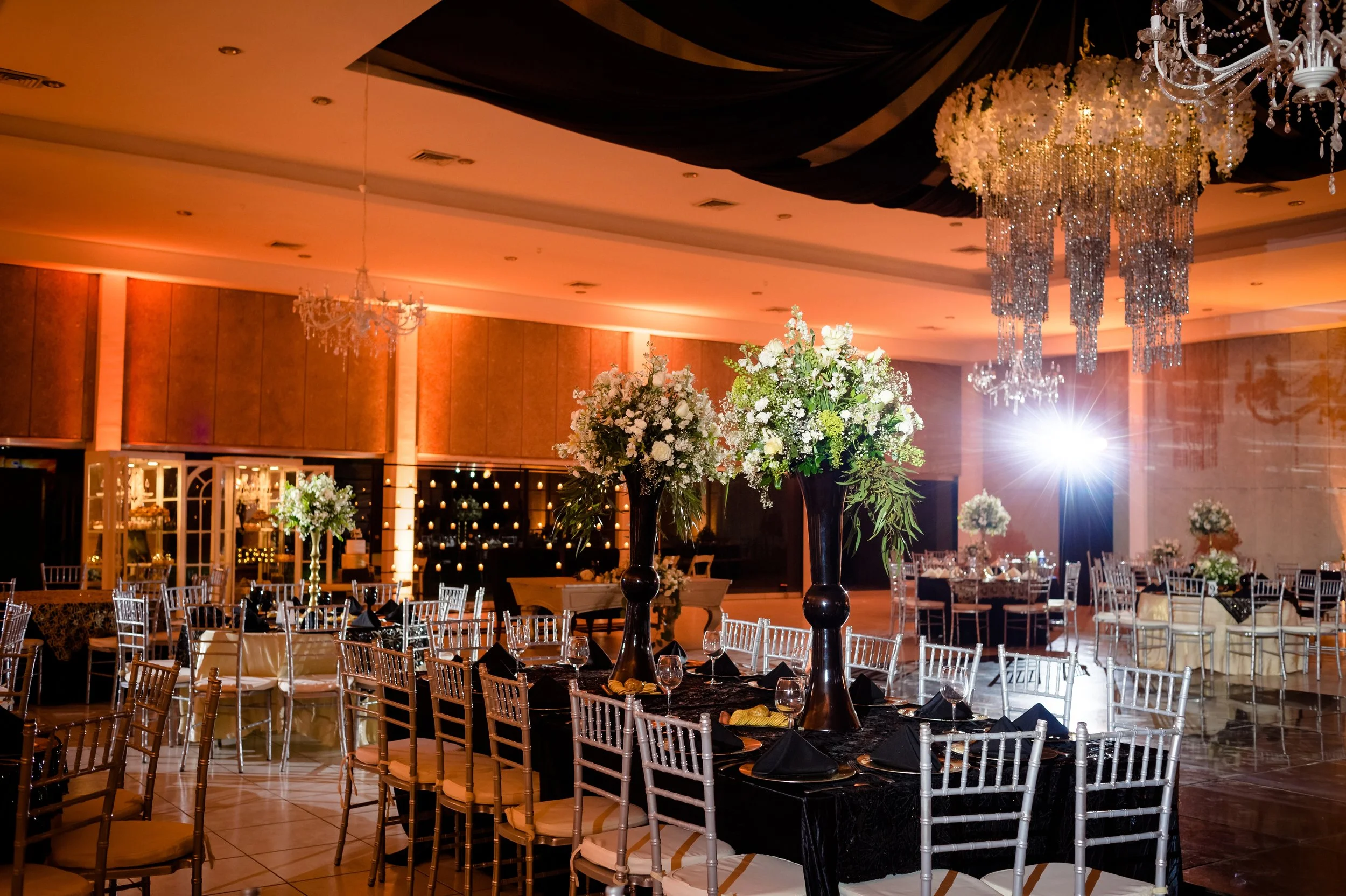 Elegant banquet hall decorated for a formal event with flower centerpieces, chandeliers, and draped ceiling fabric.