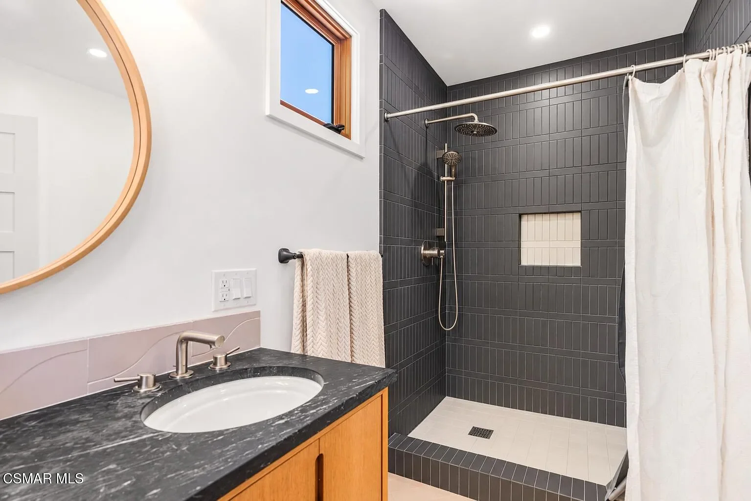 Shower fully tiled in a black, porcelain, straight stack brick with soapstone remnant on the countertop.