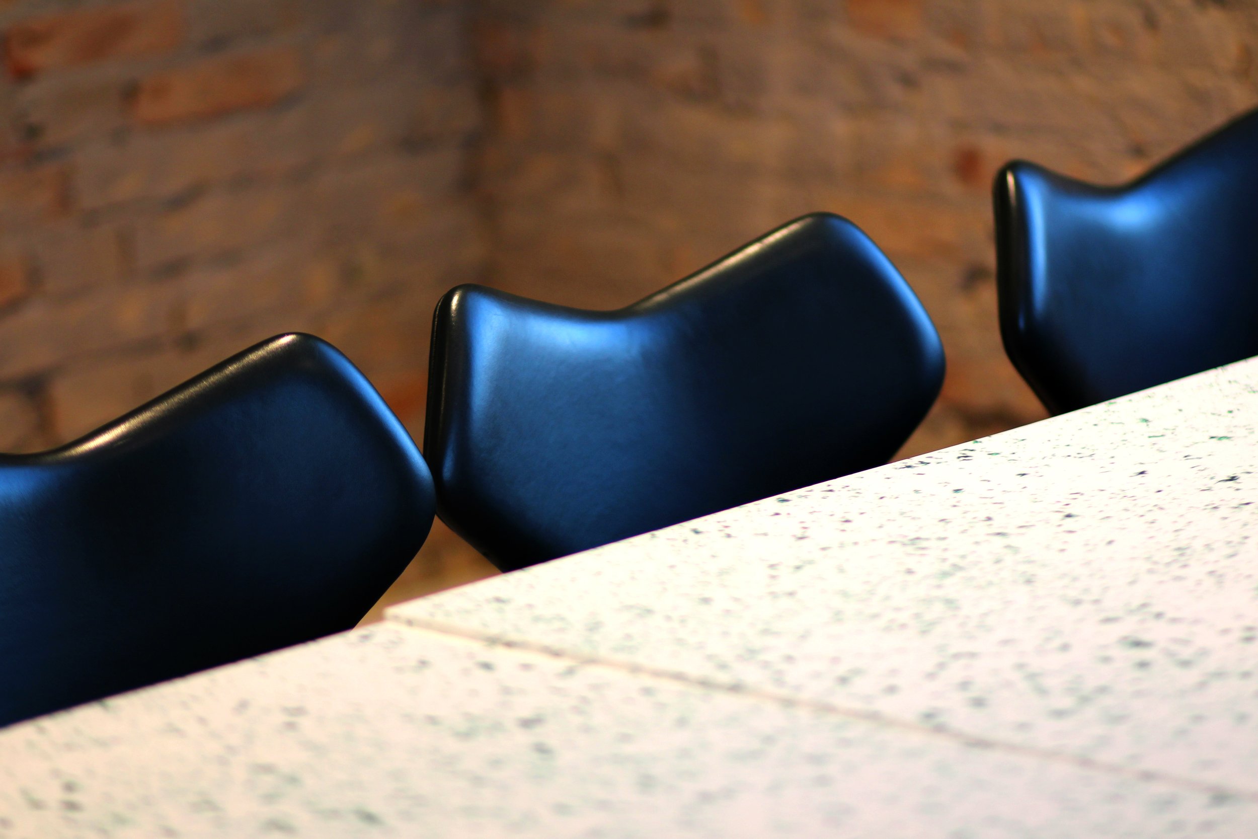 A close-up of three black chairs positioned behind a white speckled table, with a brick wall in the background.