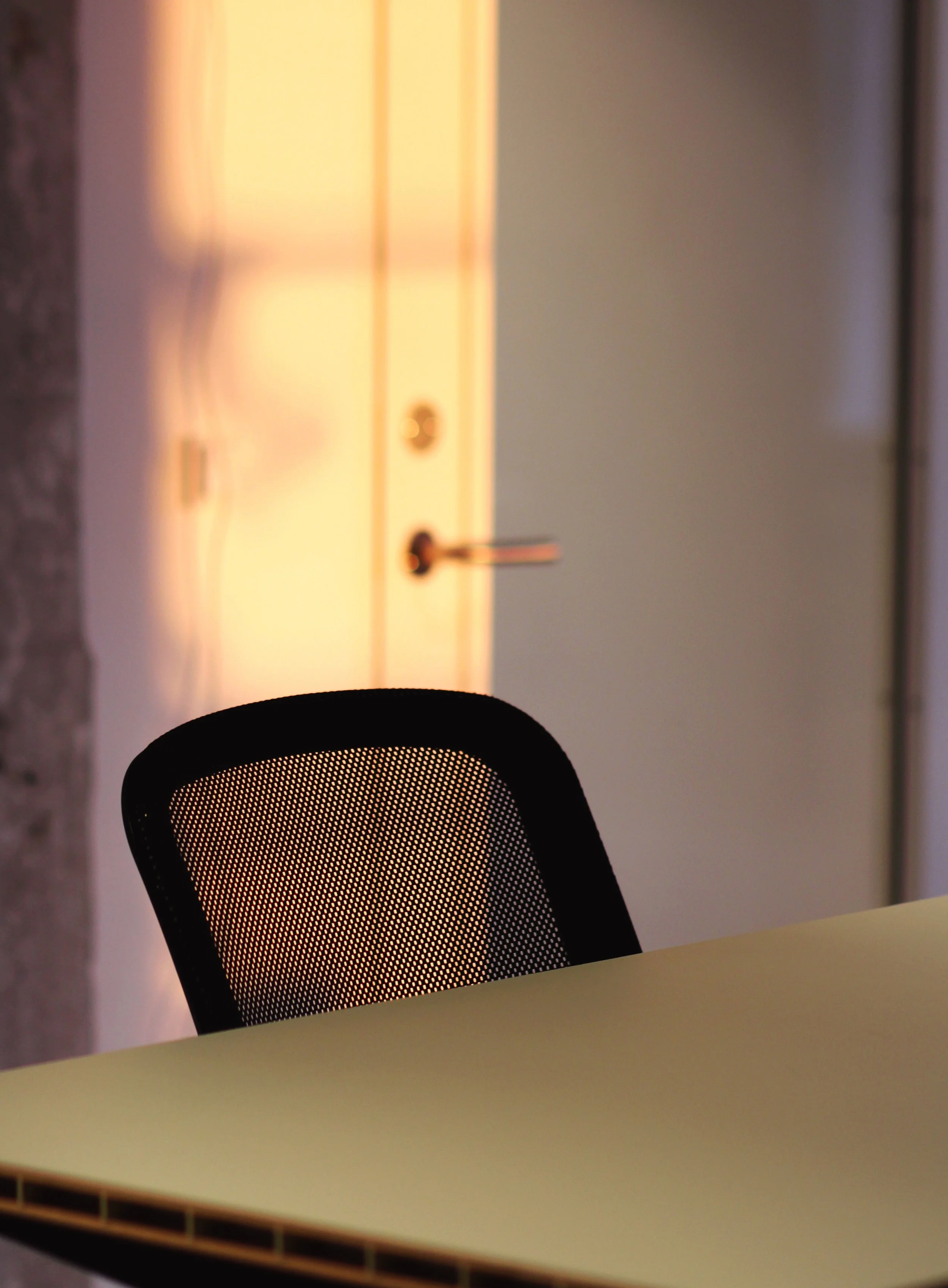 An office chair with a mesh backrest in front of a light-colored table, with a closed door in the background.