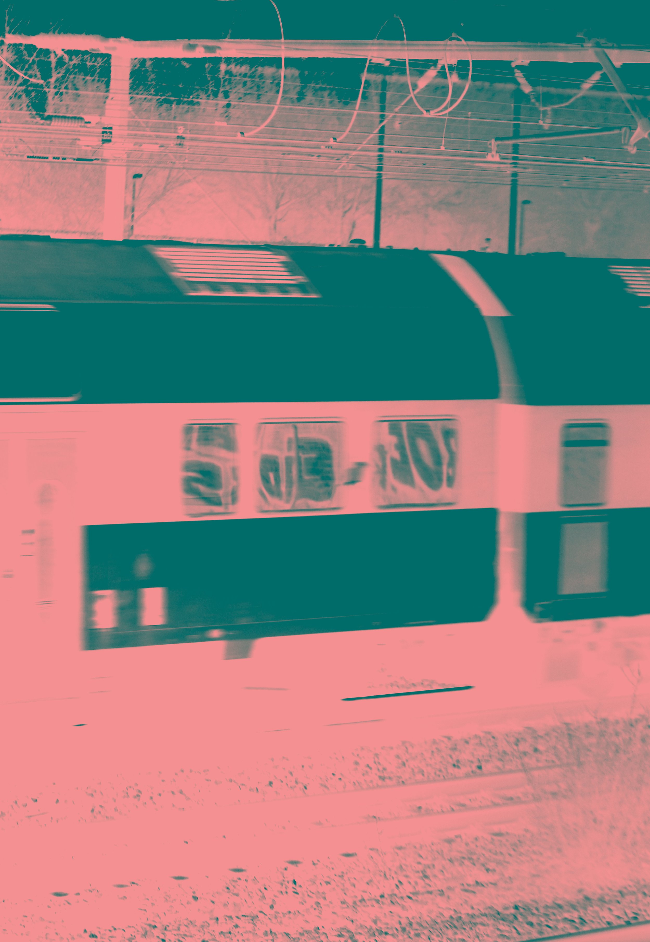 A train moving on tracks with overhead electrical wires, seen through a window with reflections.