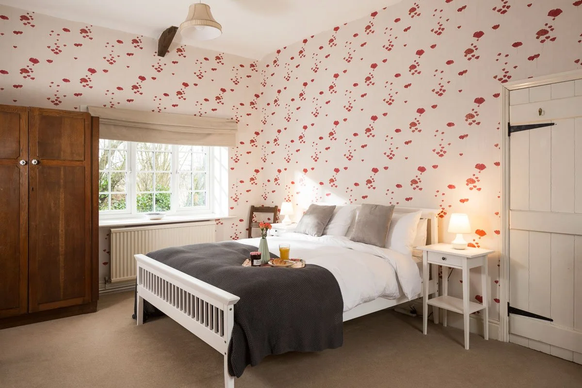 large bedroom with red and white patterned wallpaper, tall wooden wardrobe, large bed with grey bedding