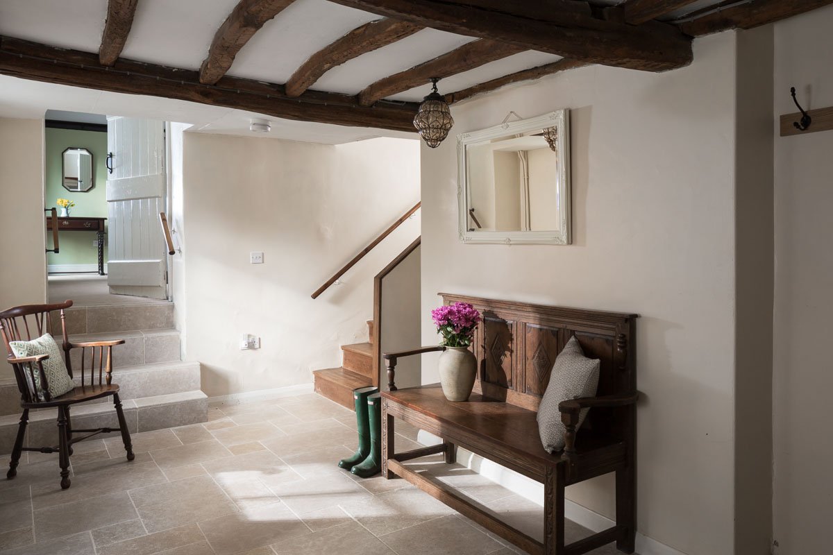 Hallway in old cottage with wooden bench seat, willies, wooden arm chair, glimpse into room beyond