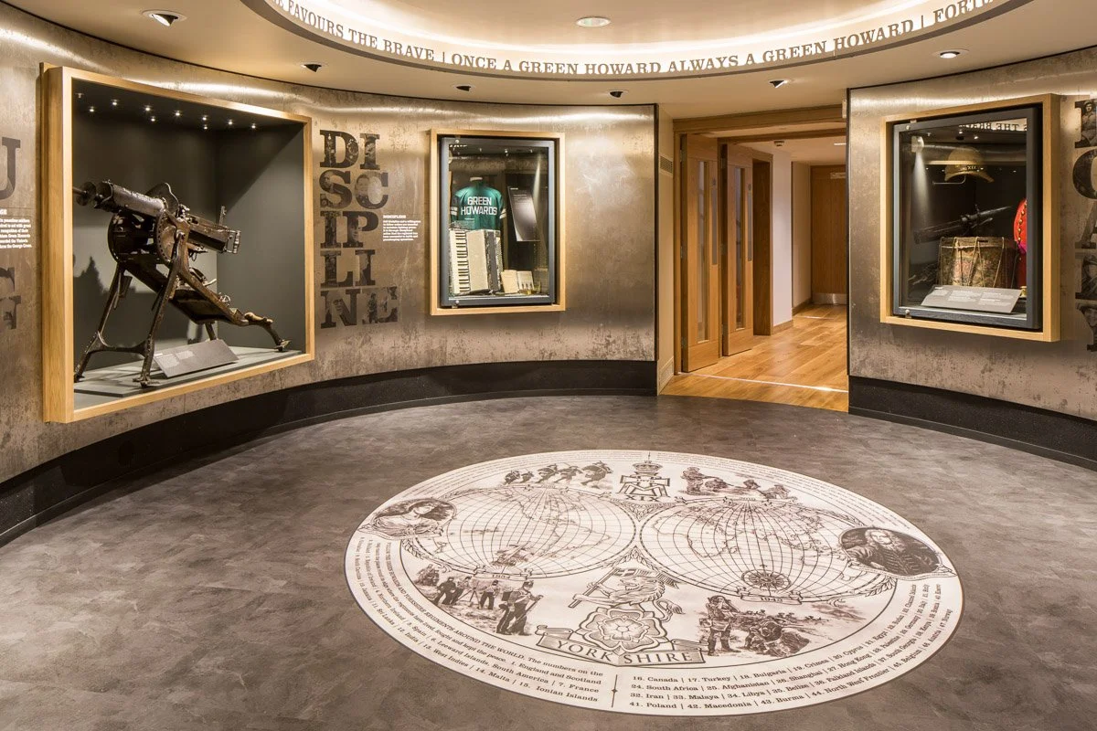 circular room in green Howards museum showcasing historical clothing and weaponry, hallway leading away