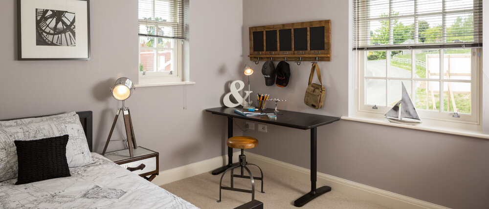  detail image of desk area in bedroom with cream carpets, tripod lamp, black desk and stool 