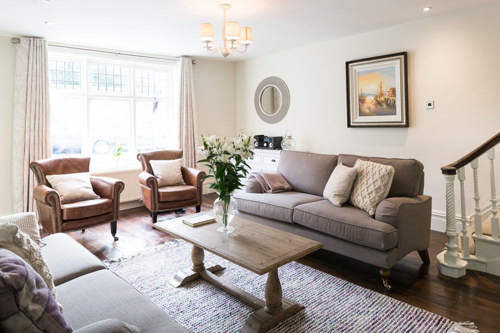  cottage living room with wooden flooring, grey sofa, leather arm chairs, large sash windows  