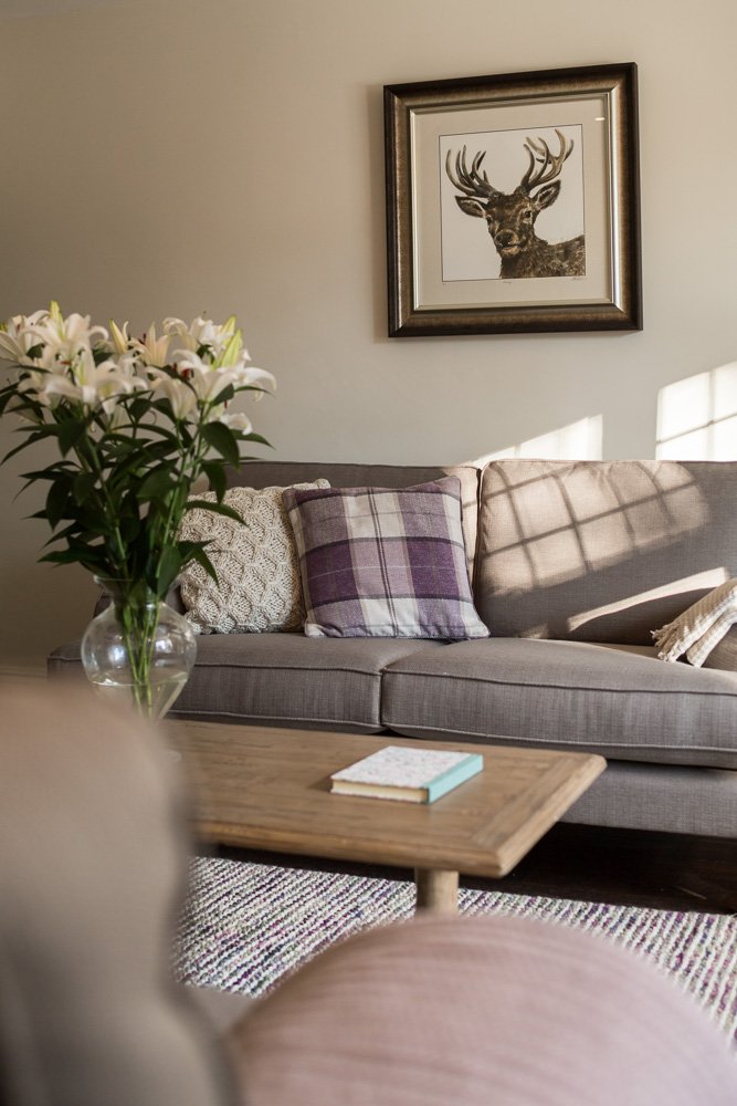  portrait image looking across coffee table with flowers on towards grey sofas with cushions  