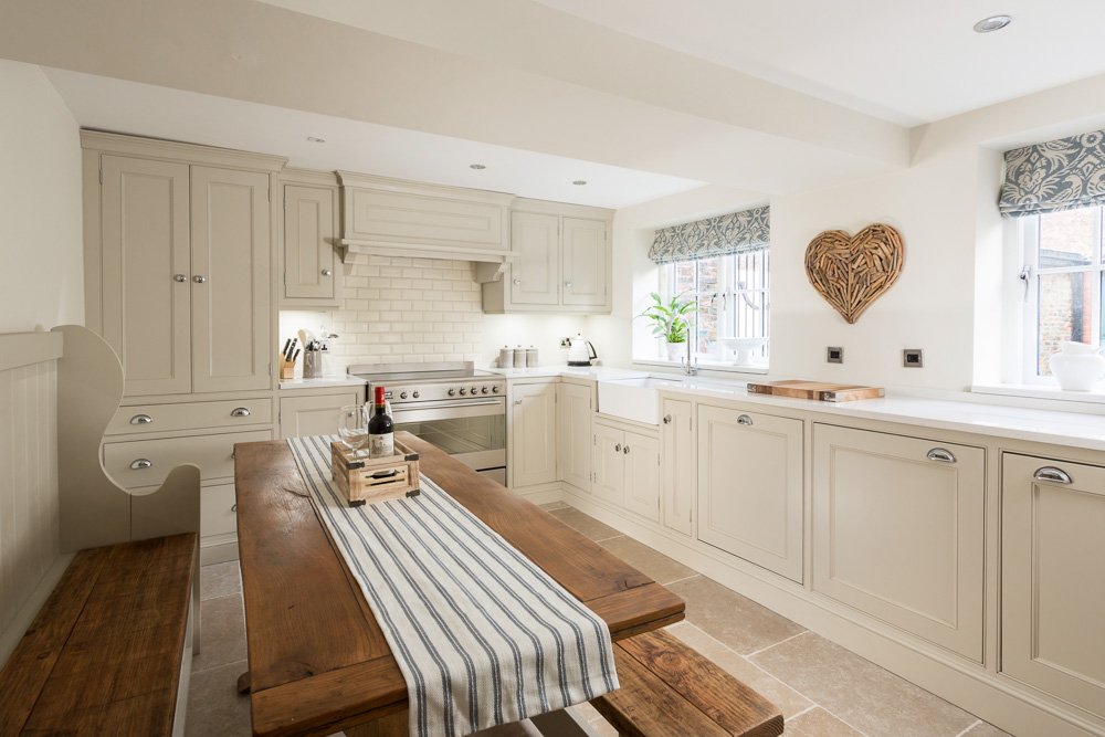  farmhouse style kitchen diner with beige tile flooring, cream units, white worktops, large range cooker, wooden dining tale with bench seats 