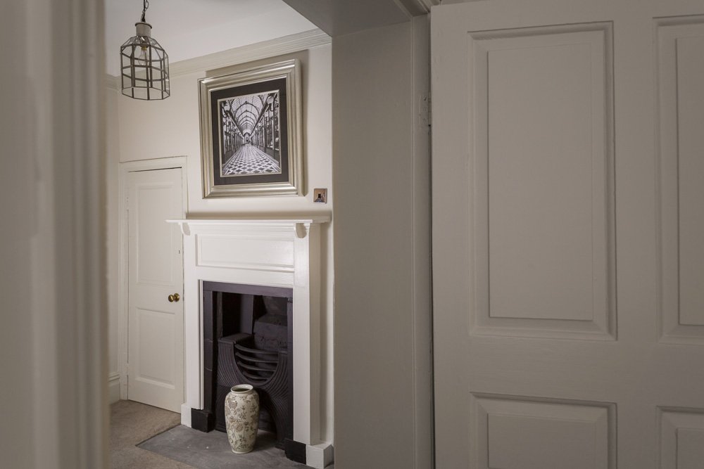  glimpse of a traditional fireplace through a doorway with an art print above  