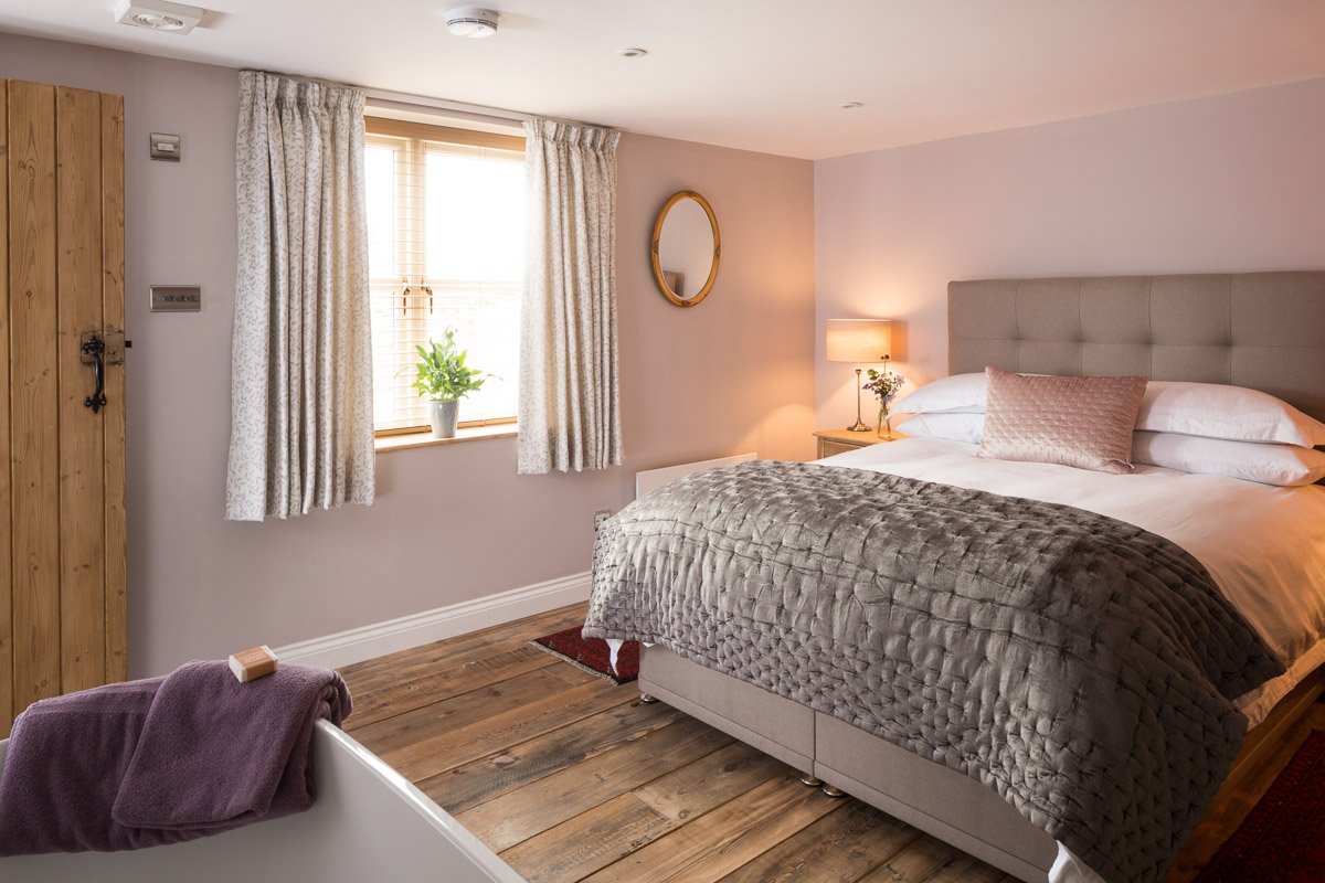  low ceiling bedroom with wooden flooring, pale pink walls, large bed, latched wooden door 
