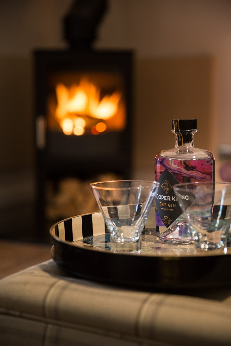  portrait image of coffee table with drinks tray including gin bottle and glasses, roaring log burner out of focus behind  