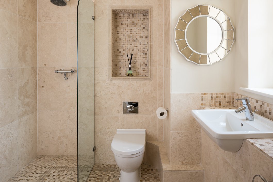  one point perspective of bathroom well lit, beige tile walls and flooring  