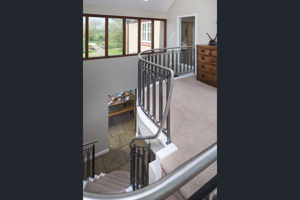  well lit image of landing and looking down spiral staircase with glimpse into breakfast room below and views out of the first floor windows  