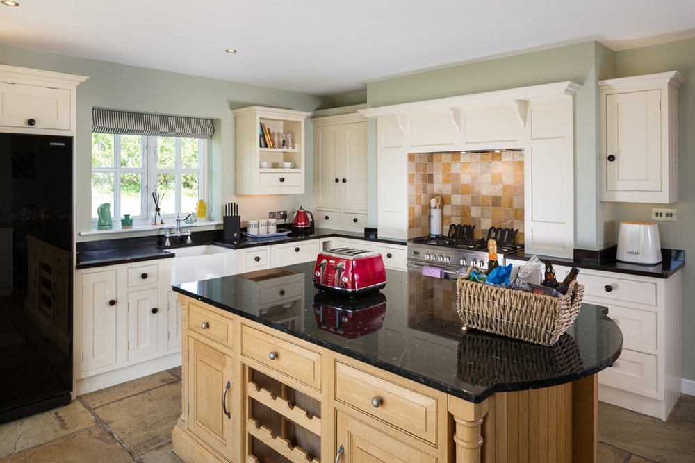  well lit image of kitchen with wooden and white units, black countertops, large range cooker and hamper basket on island  