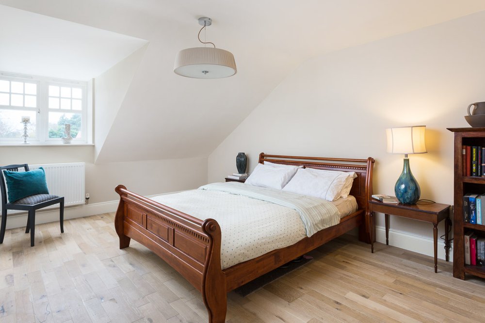  well lit bedroom with wooden sleigh bed, pale wooden flooring, white walls, small wooden chair to the left 