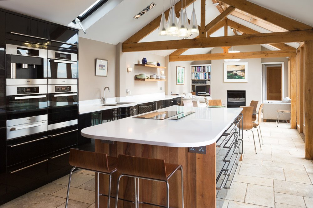  well lit long kitchen diner with black nits, white counter tops, beamed ceiling with sky lights 