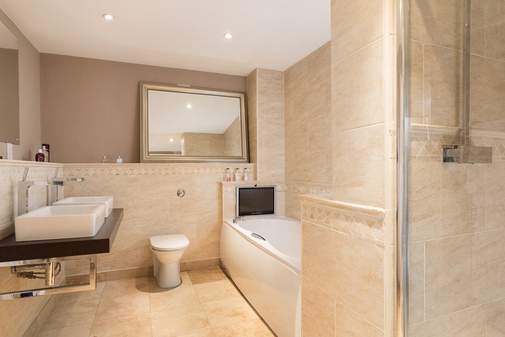  well lit bathroom with beige tile flooring and walls, large mirror and dark sink unit  