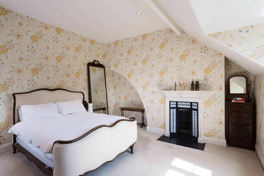  lofted ceiling bedroom with yellow flower pattered wall paper, traditional fireplace, sky light  