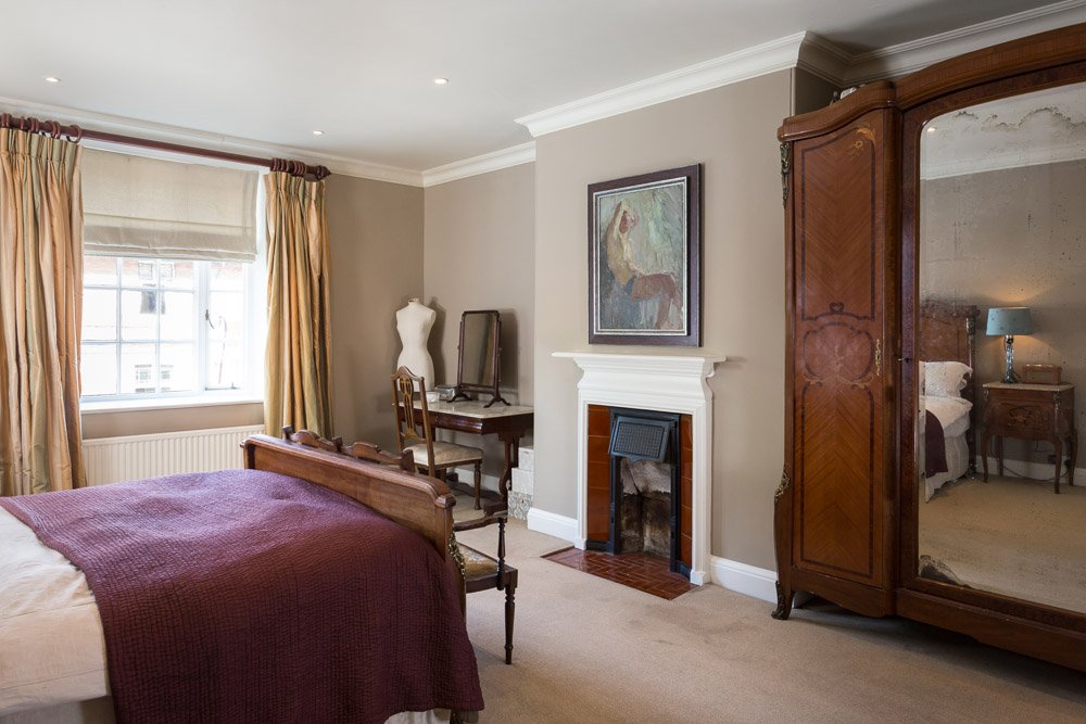  bedroom with dark cream walls, cream carpet, burgundy bedding, large sash window, traditional fireplace 