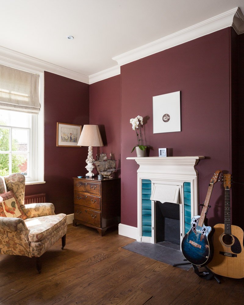  burgundy bedroom with wooden flooring, arm chair on left, sash window, traditional fireplace  