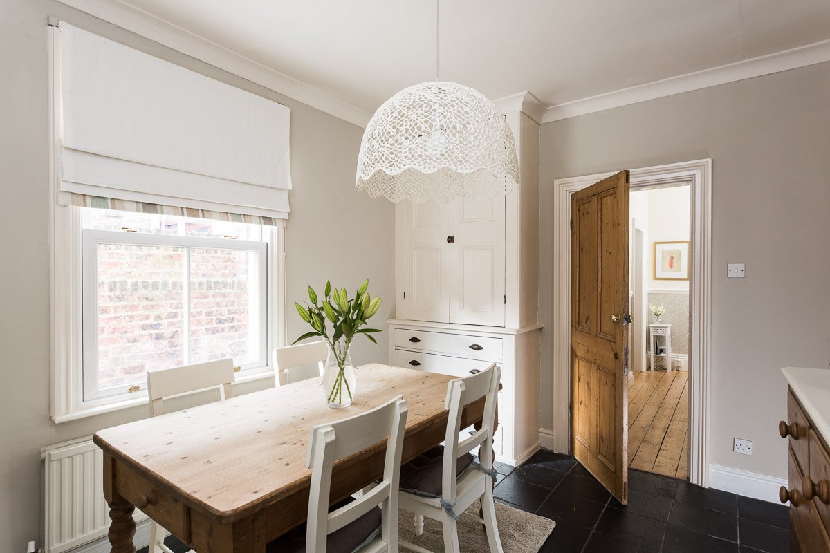  farmhouse style dining room with wooden dining table, sahs window, dark tile flooring, glimpse into hallway beyond 