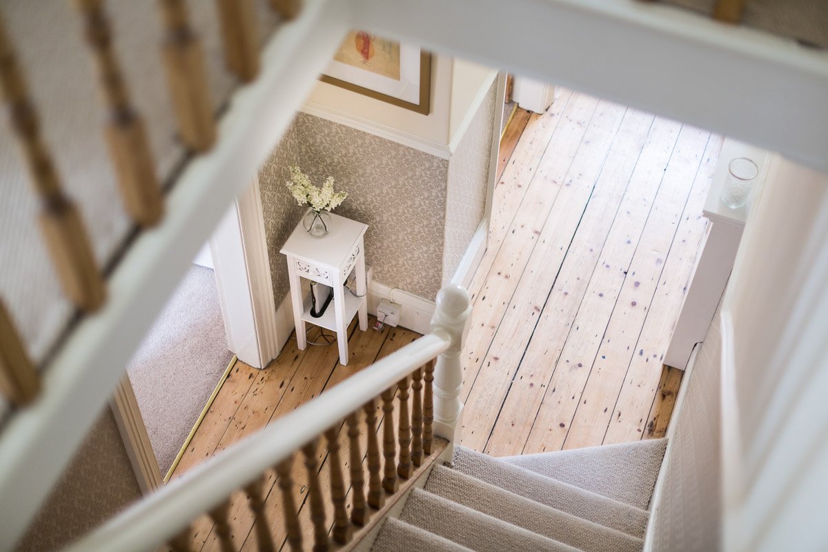  image looking down the stairs towards hallway, wooden flooring, carpet runner, small table with flowers 