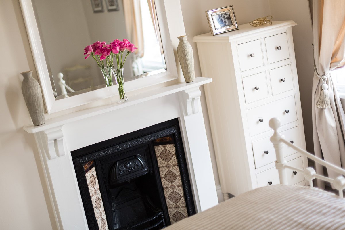  detail shot across bed of traditional fireplace with flowers on the mantlepiece  