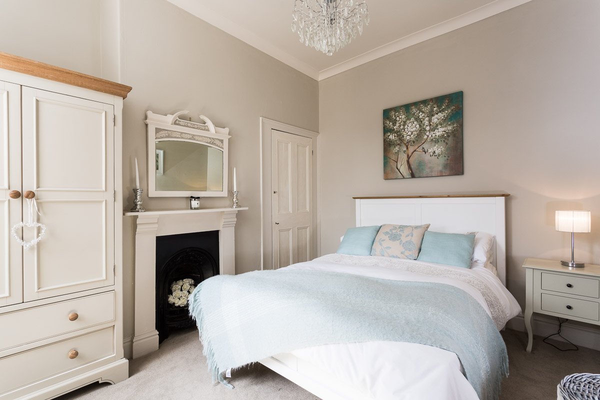  high ceiling bedroom with pale grey walls, blue bedding and traditional fireplace  