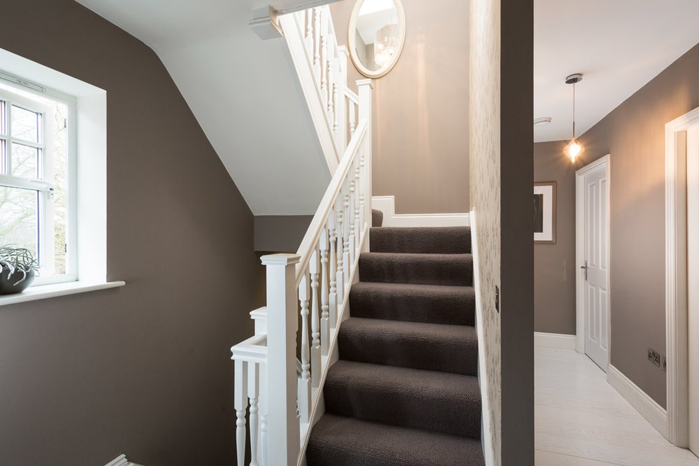  well lit hallway with stairs going up and down, grey walls, white carpet, grey stair runner 