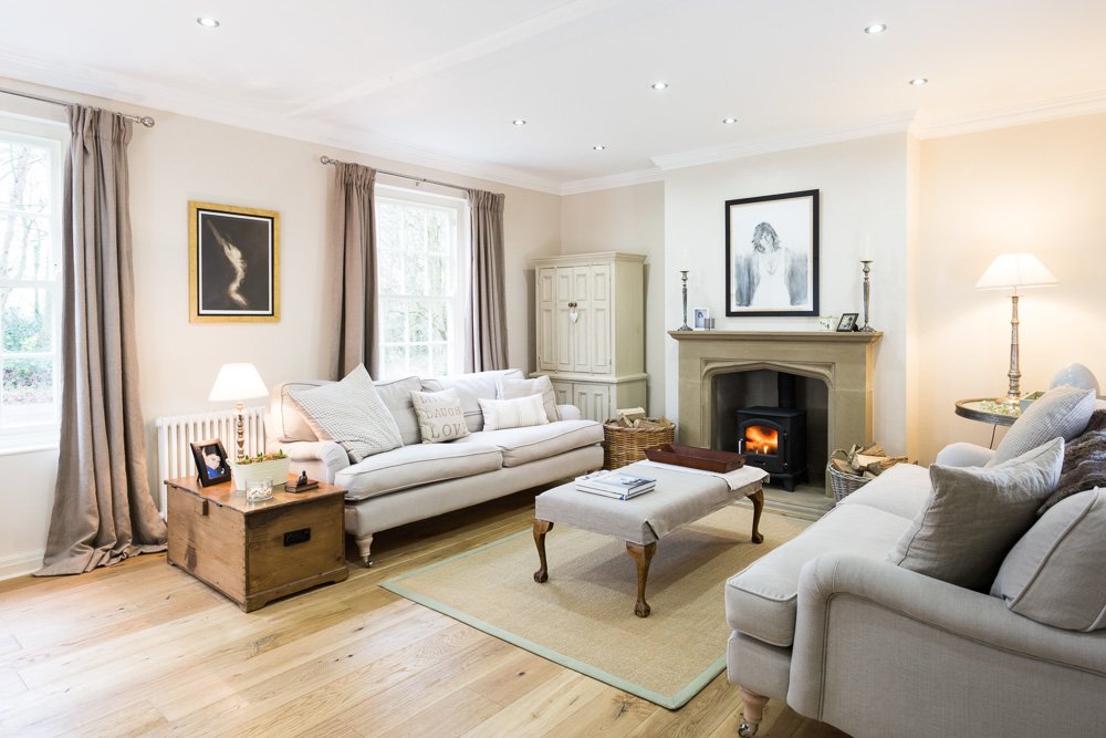   large living room with white walls, wooden flooring, fire place with log burner, cream sofas   