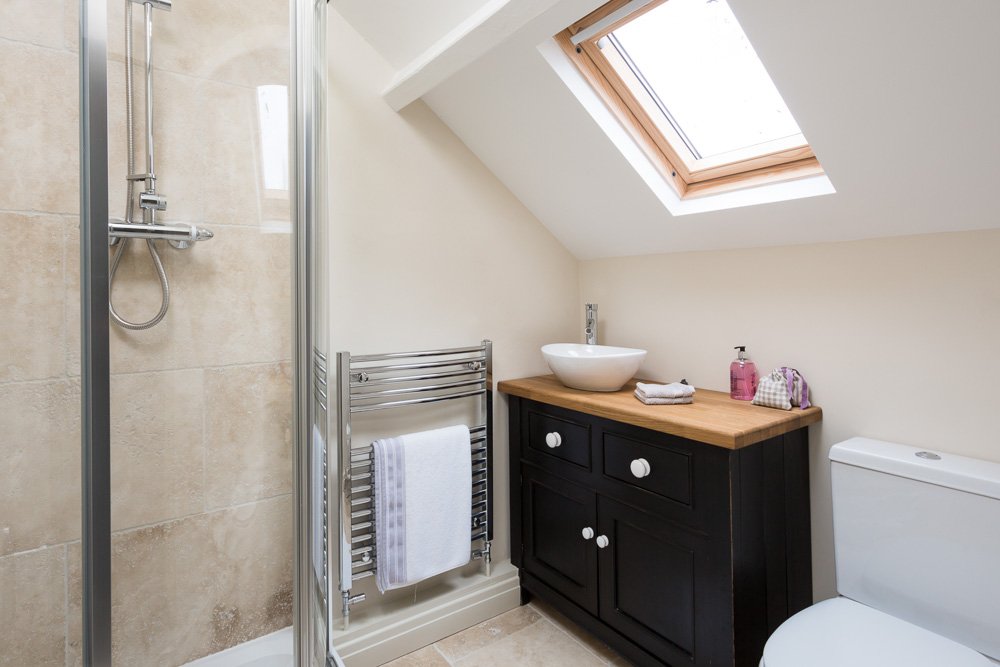  lofted ceiling bathroom with black sink unit, beige floor and wall tiles, skylight 