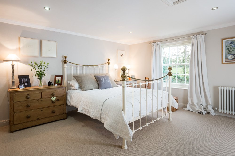 large bedroom with tall metal frame bed, pale grey walls, beige carpet, white bedding  