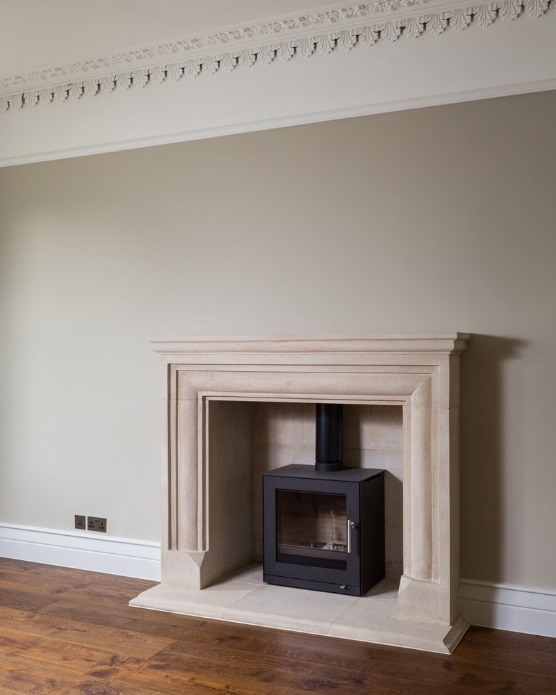  detail of carved stone fireplace with log burner, sage green walls, wooden flooring 