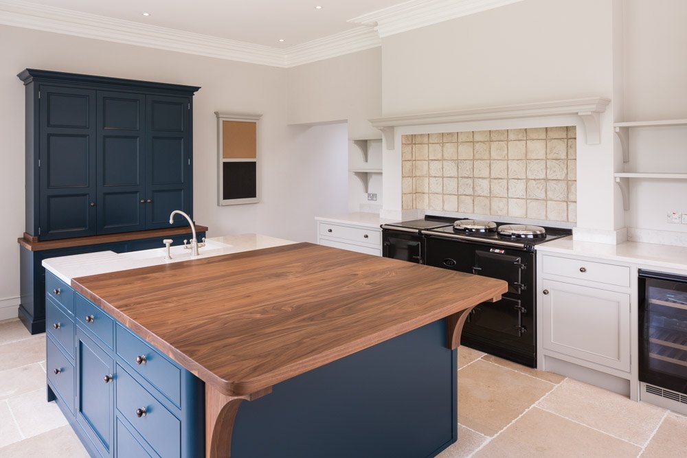  newly fitted kitchen, navy units, white counter tops, black aga and beige tile flooring 