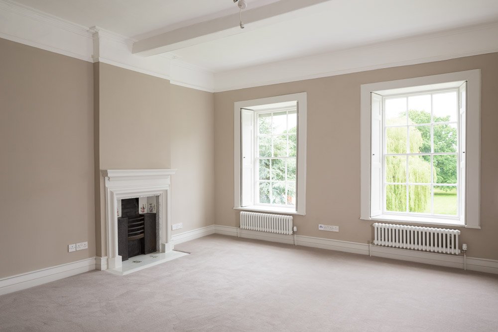  large high ceiling room with dark beige walls, large sash windows, cream carpet, traditional fireplace 