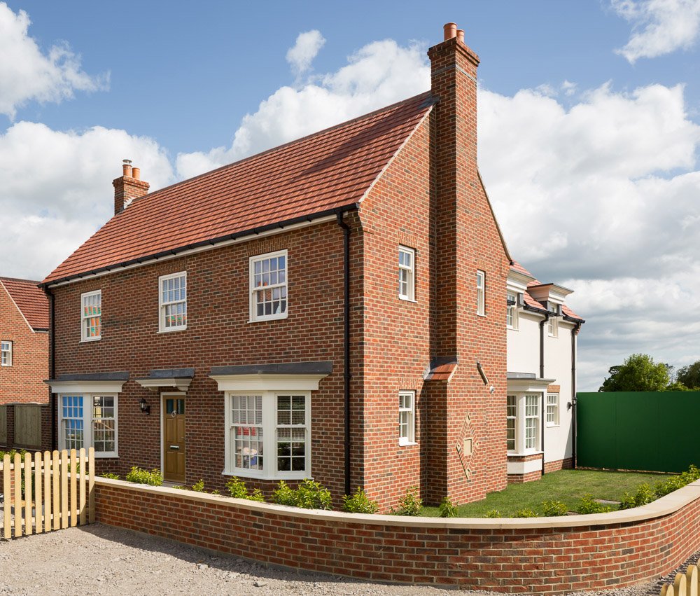  3/4 image of new build red brick home with small walled front garden and driveway  