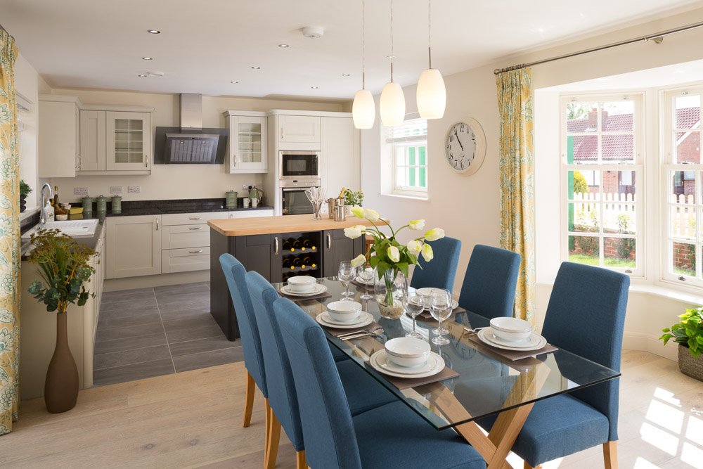  dining area with glass dining table, blue chairs, pendant lights and modern kitchen in the background  
