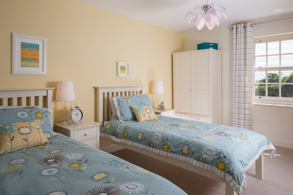  twin bedroom with powder yellow walls, blue bedding and large window 