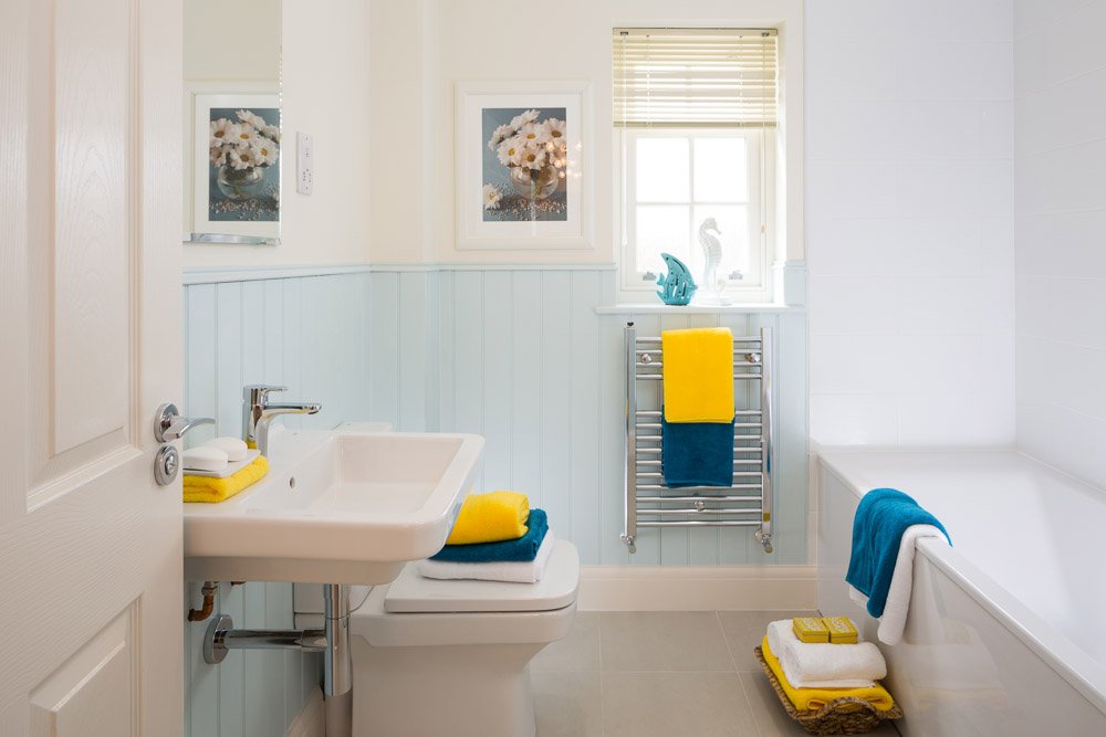  bathroom with powder blue panelling, blue and yellow towels on bath, towel rail and toilet seat 