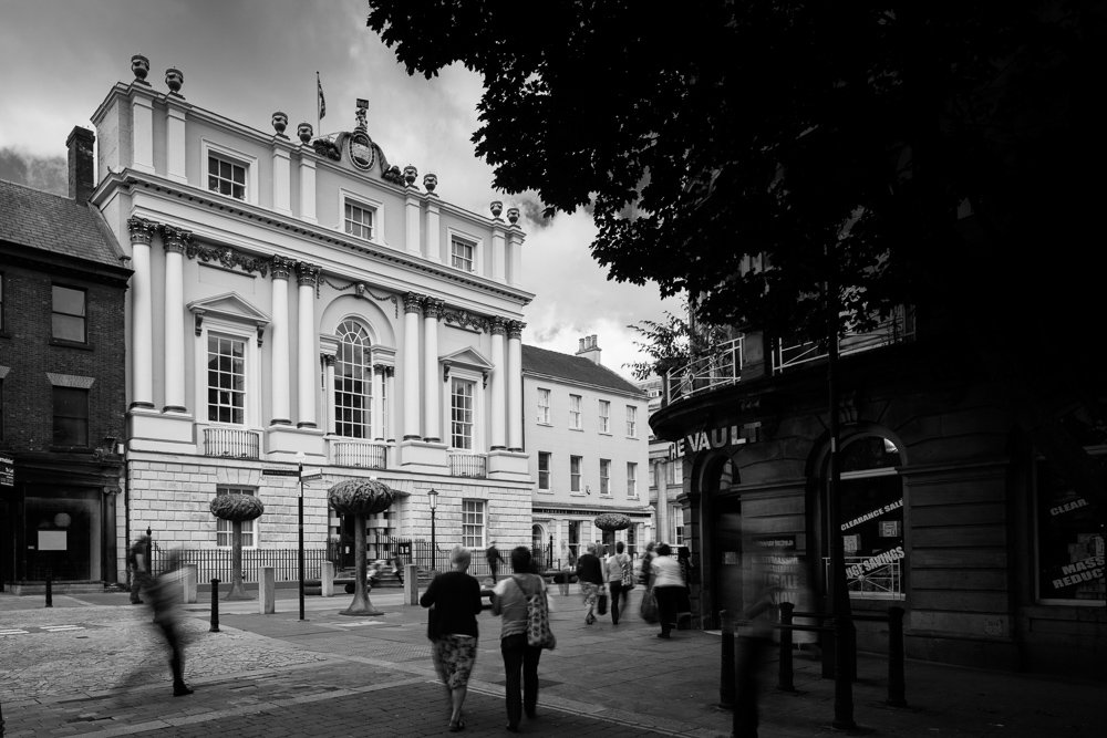  black and white street scene of Doncaster Mansion House in the sun with pedestrians walking past below  