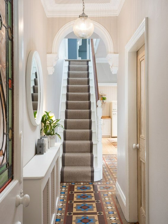  overexposed hallway with stained glass door, traditional tile flooring, white wooden stairs with carpet runner, kitchen can just be seen in the background  