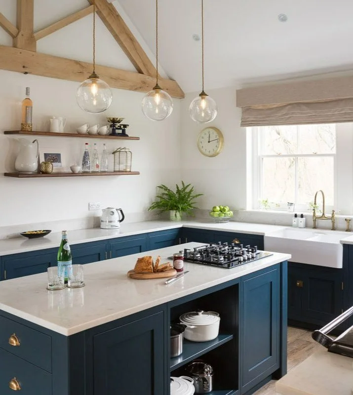 portrait image of high beamed ceiling with navy units, white worktops and pendant lights 
