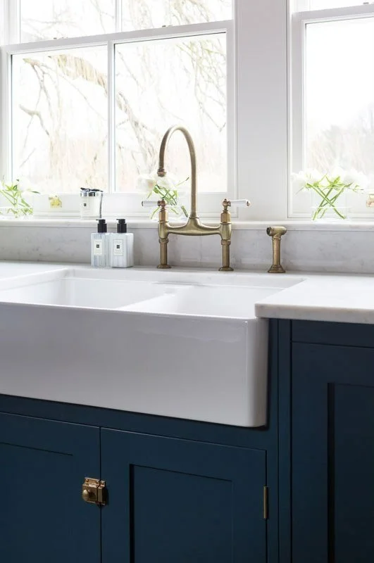 detail shot of large porcelain sink with brass tap, navy units and white worktops