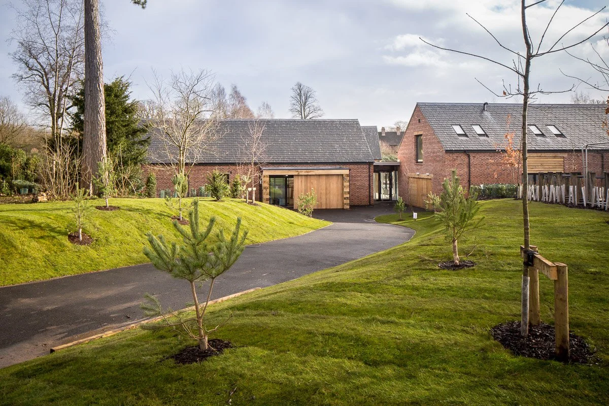 dunham massey visitor centre, long winding driveway leading to two new brick barn style buildings 