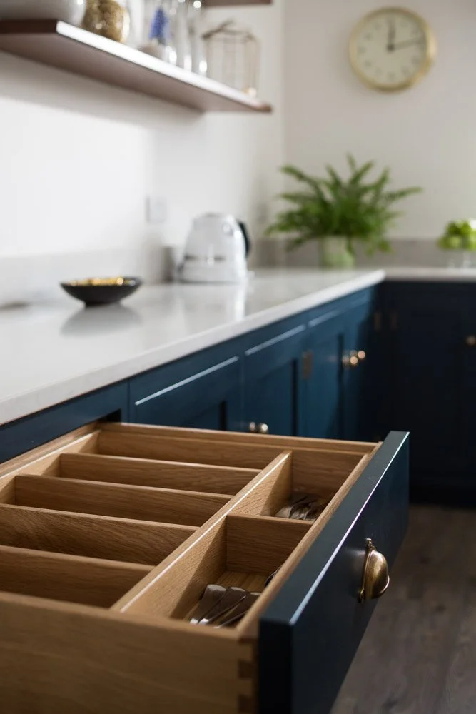 detail shot of open kitchen draw with cutlery dividers, white worktops, navy units