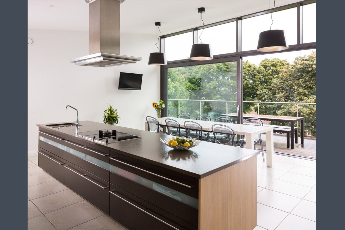 modern kitchen with tile flooring, dark units, pendant lights, full height glass wall with balcony beyond 