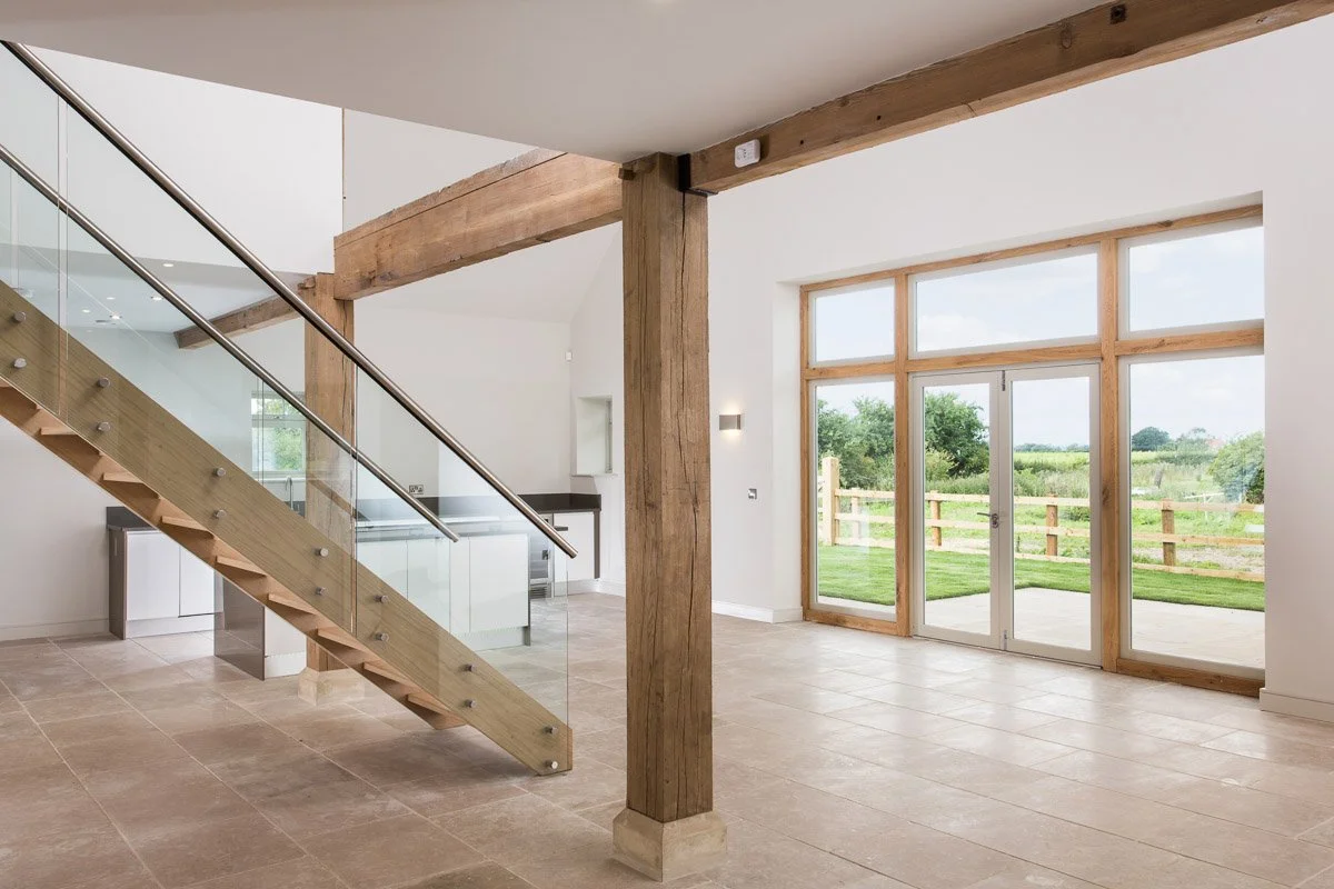open plan double height ceiling kitchen diner, wooden stair case with glass banister, wooden pillars, large glass doors leading to garden